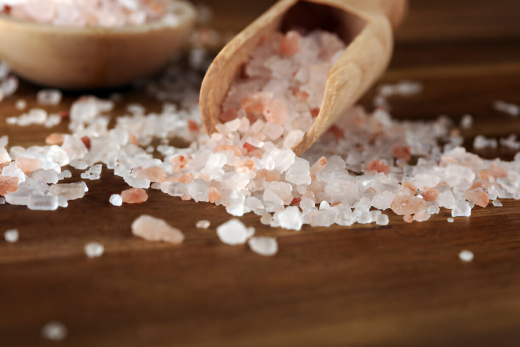 A wooden spoon rests on a table, filled with pink salt, showcasing its vibrant color and natural texture.